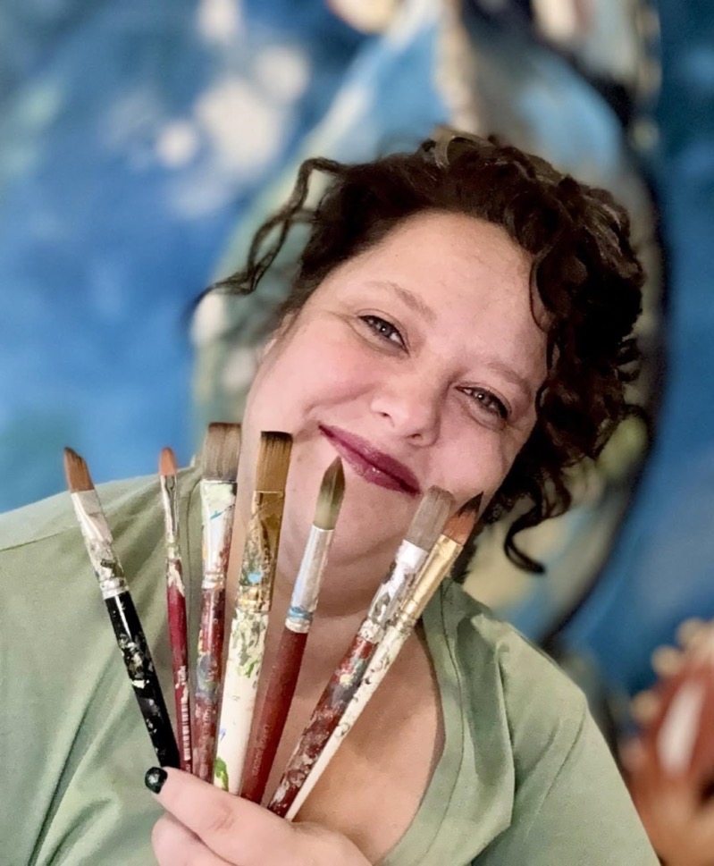 Rachel Vinson holding a fan of well-used paintbrushes.